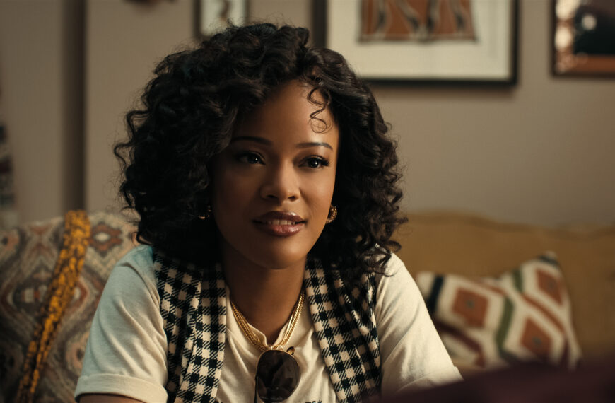 "A young woman with curly hair sits on a patterned couch in a cozy living room, wearing a checkered vest and white shirt, with framed art and cushions in the background, engaged in conversation."